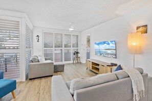 A modern living room with a sofa, TV, and a lamp. - Wyuna Coastal Escape - 3BR Apartment (Gold Coast)