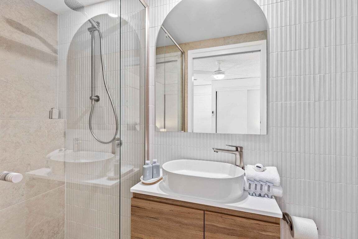 A modern bathroom with a glass-enclosed shower, a round sink, and a mirror above the vanity.