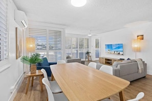 A modern living room with a dining table, sofas, and a TV. - Wyuna Coastal Escape - 3BR Apartment (Gold Coast)