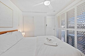 Ein Hotelzimmer mit einem Bett, einem Deckenventilator, einer Tür und einem Fenster mit Jalousien.