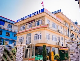 Um hotel com um letreiro grande de 'CAUTAM HOTEL', várias janelas e uma entrada com portão.