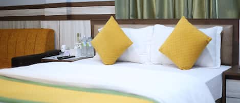 A hotel room with a bed, two pillows, a bedside table, a chair, and a window with curtains.