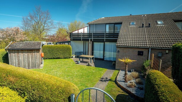 Ein modernes Haus mit einem gepflegten Garten, einem Holzschuppen und einer Terrassenfläche.