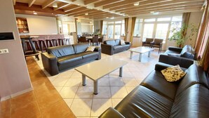 A spacious living area with leather sofas, a coffee table, and a dining area with chairs and a table. - Coastal Group Lodge for 40 Guests (Ellemeet)