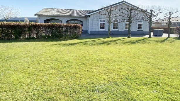A two-story building with a sloped roof, a hedge, and a well-maintained lawn. - Coastal Group Lodge for 40 Guests (Ellemeet)