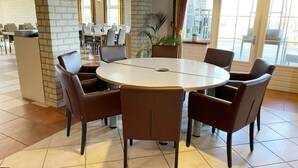 A conference room with a round table, brown chairs, and a potted plant. - Coastal Group Lodge for 40 Guests (Ellemeet)