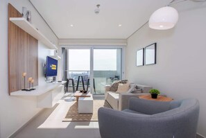 A modern living room with a sofa, coffee table, TV, and a balcony with a city view. - Corporate Stays First Living - 703 (Asunción)