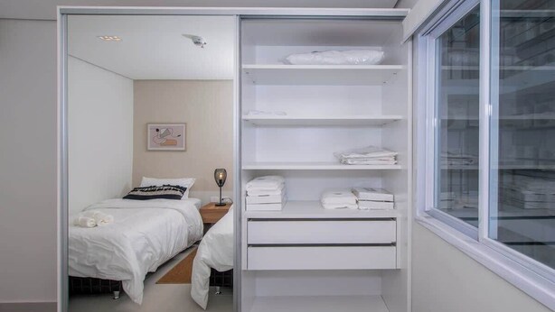 Un dormitorio con cama, mesita de noche, espejo y armario con estantes.