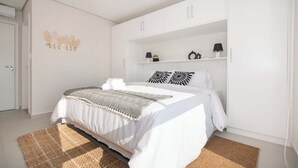 Ein Schlafzimmer mit einem Bett, einem weißen Kleiderschrank, Regalen mit Gegenständen und einer Wanddekoration.
