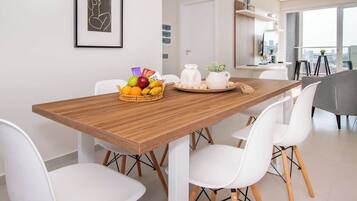 Un comedor moderno con una mesa de madera, sillas blancas, una cesta de fruta y una jarra sobre la mesa.
