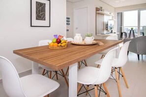 Un comedor moderno con una mesa de madera, sillas blancas, una cesta de fruta y una jarra sobre la mesa.