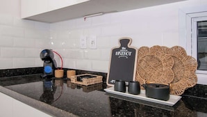 Una encimera de cocina con una cafetera, un posavasos tejido y un letrero de pizarra.