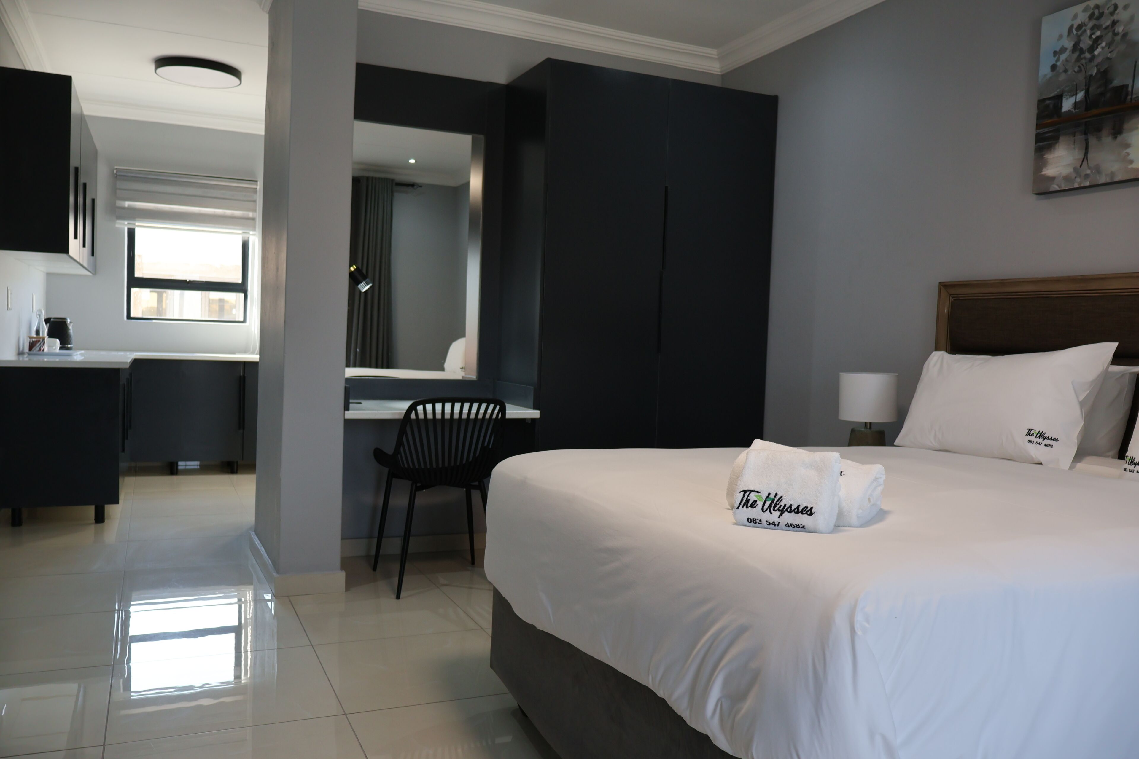 A hotel room with a bed, a desk, a chair, a mirror, and a painting on the wall.