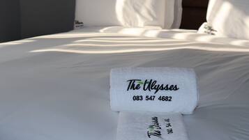 Ein ordentlich bezogenes Bett mit weißen Laken und einem Handtuch, das den Hotelnamen 'The Alyses' und die Telefonnummer zeigt.