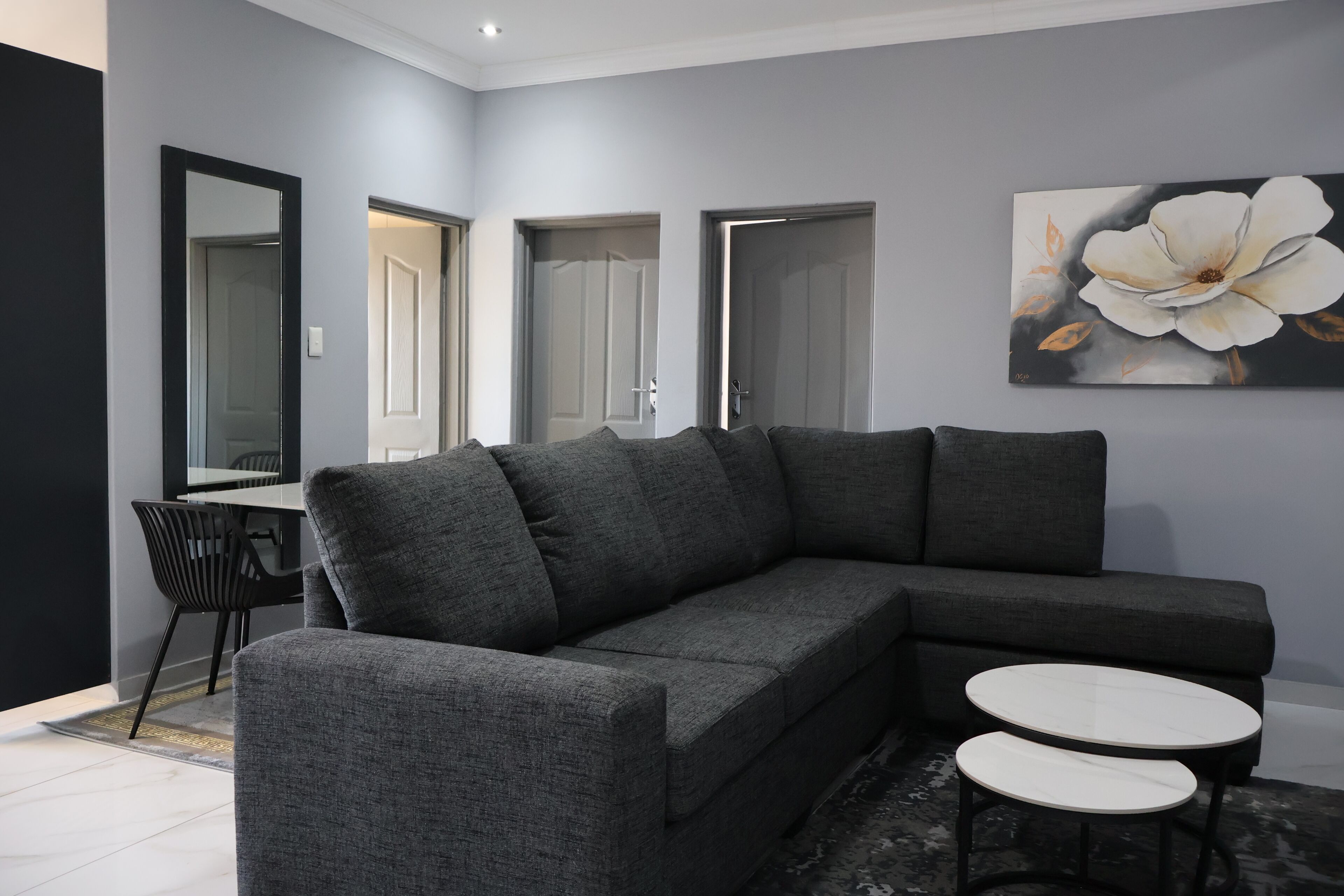A modern living room with a grey sectional sofa, two round tables, and a large floral painting on the wall.