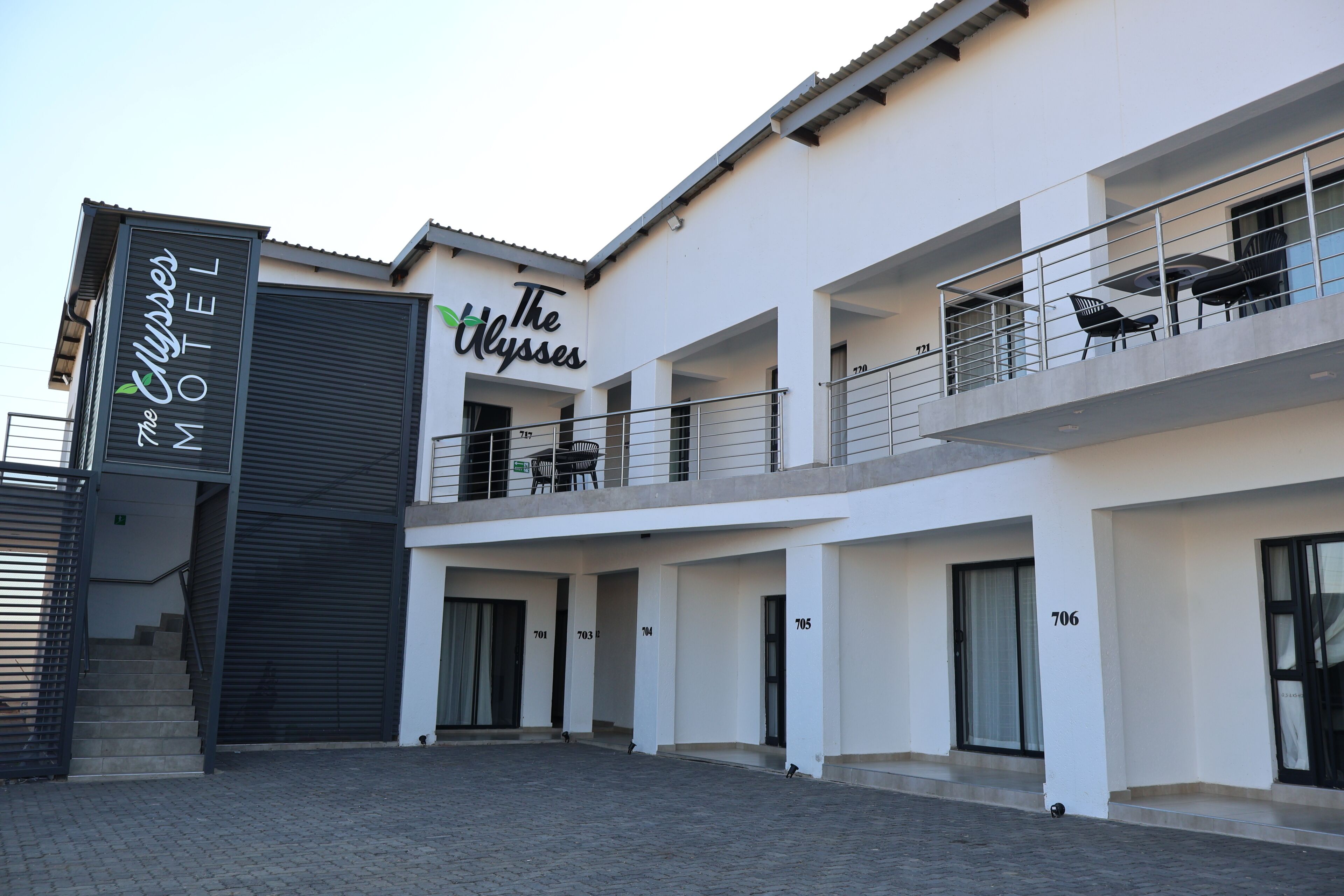 A modern hotel with a sign reading 'The Ulysses Motel.' It features a ground floor with a covered entrance and a second floor with balconies.