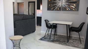 A modern living room with a grey sofa, a dining table with two chairs, and a marble floor.
