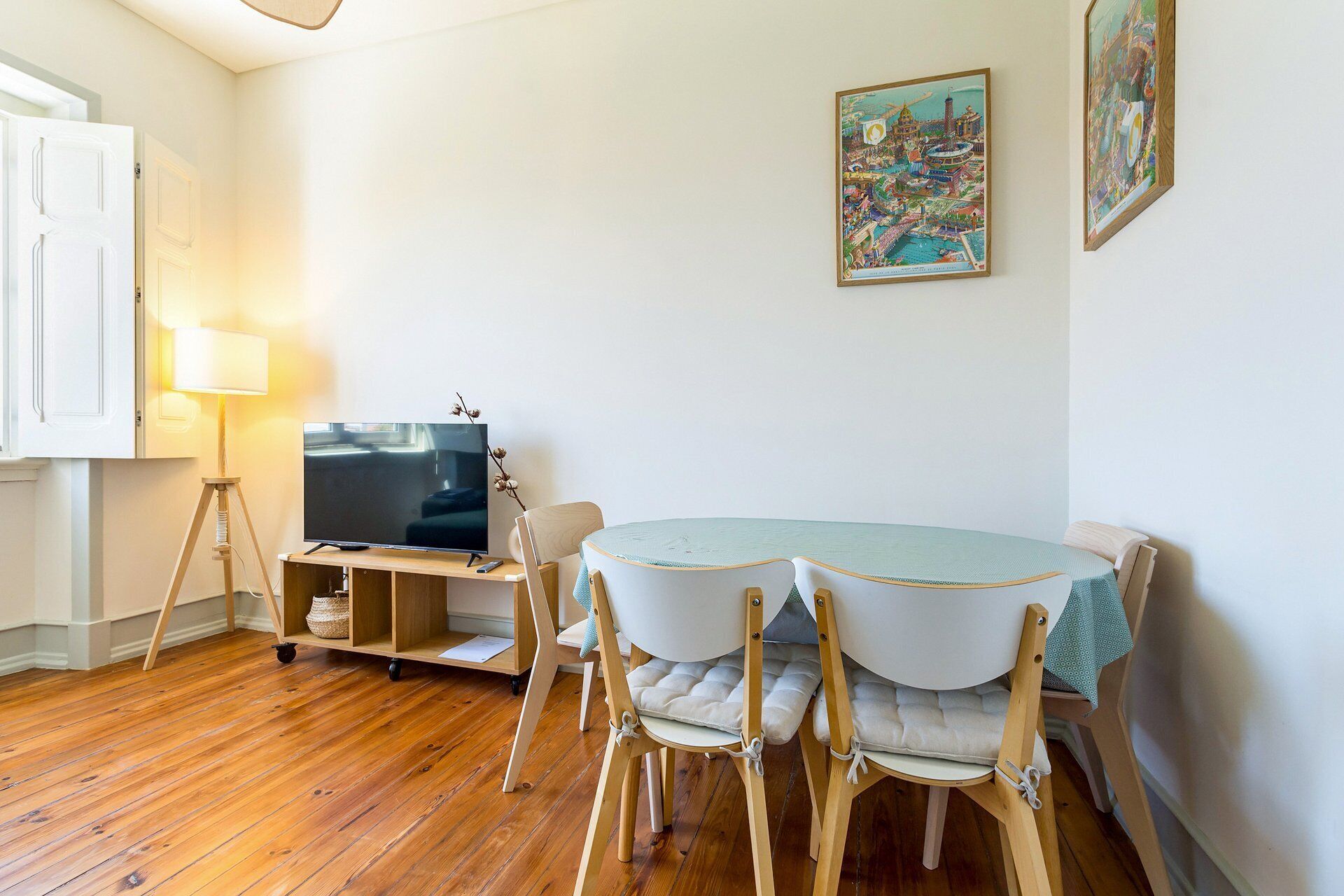 A dining area with a table, chairs, a television on a stand, and wall-mounted artwork.