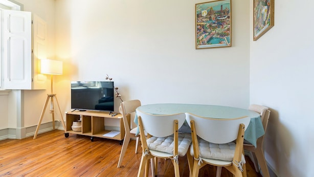 A dining area with a table, chairs, a television on a stand, and wall-mounted artwork. - GuestReady-Charming 3-Bedroom Lisbon Retreat (Lisbon)