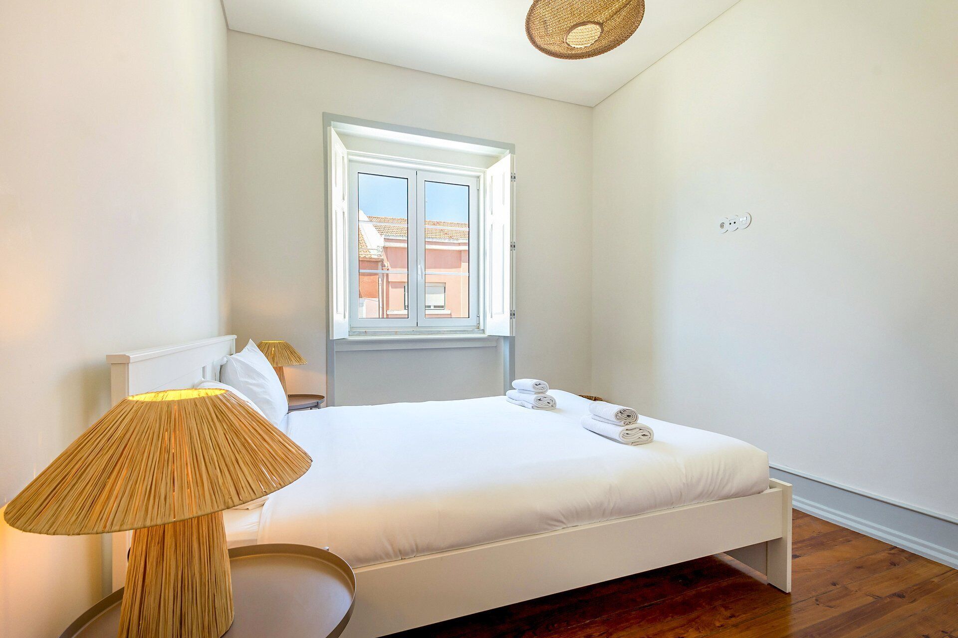 A bedroom with a bed, a window, a lamp, and a view of buildings outside.