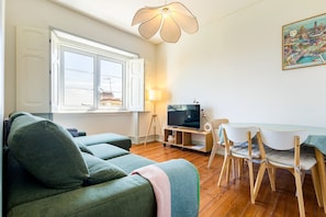A living room with a sofa, a TV on a stand, a dining table with chairs, and a window with curtains. - GuestReady-Charming 3-Bedroom Lisbon Retreat (Lisbon)