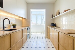 Een smalle keuken met witte kastjes, een zwarte kraan en een vloer met een patroon.