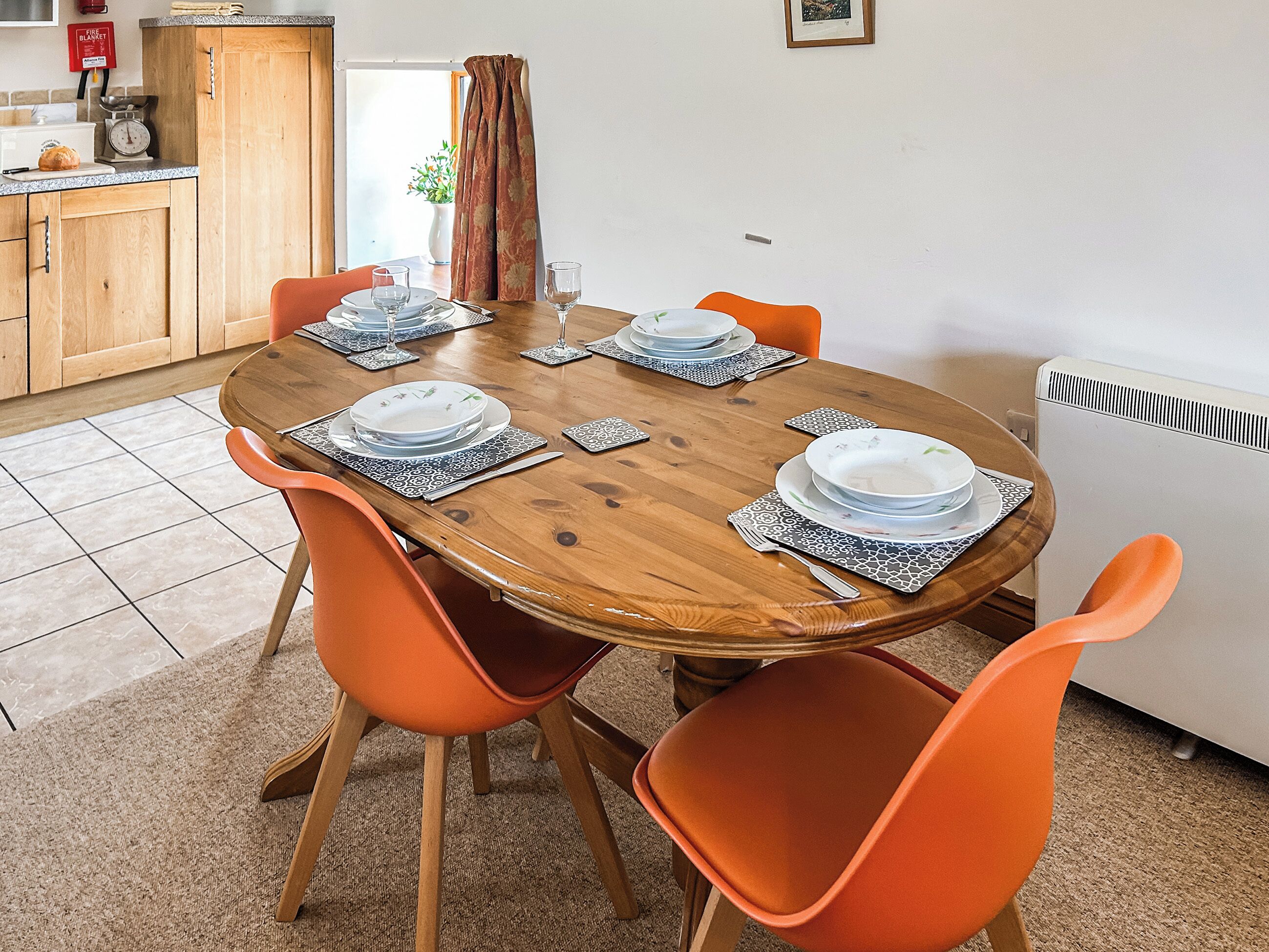 A dining table with orange chairs, a wooden table, and a kitchen area with cabinets and a radiator.
