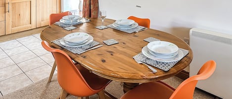 A dining table with orange chairs, a wooden table, and a kitchen area with cabinets and a radiator.