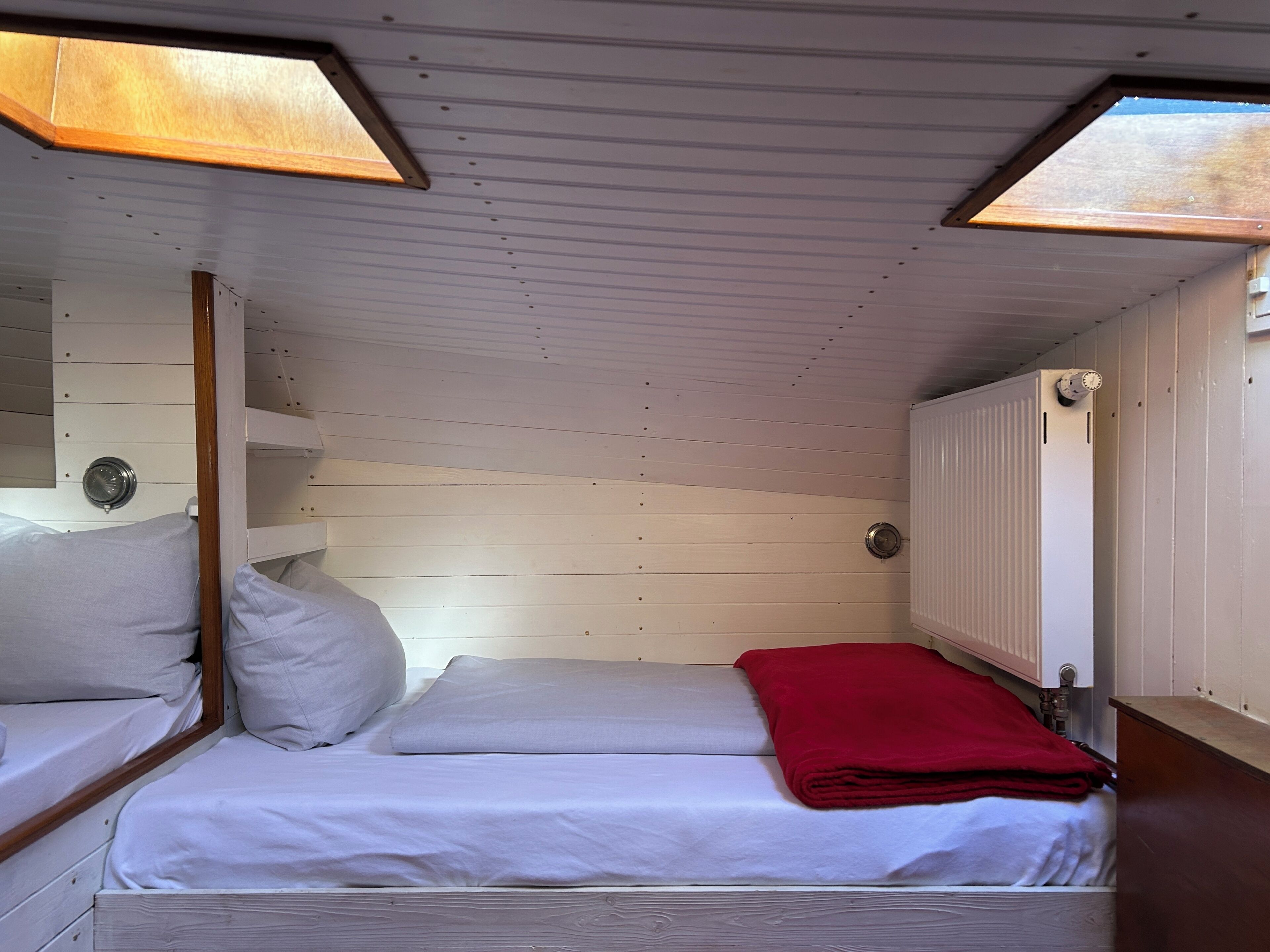Ein kleines Zimmer mit einem Einzelbett, schrägem Dach, Holzwänden und einem Fenster.