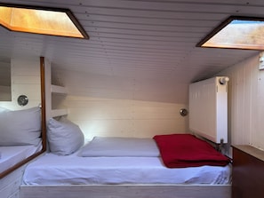 A small, single-bed room with a sloped ceiling, wooden walls, and a window.