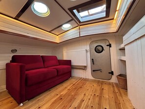 A cozy room with a red sofa, wooden flooring, a white radiator, and a skylight. - Hausboot Jonathan: Sanftes Schaukeln statt Alltagsstress (Hamburg)