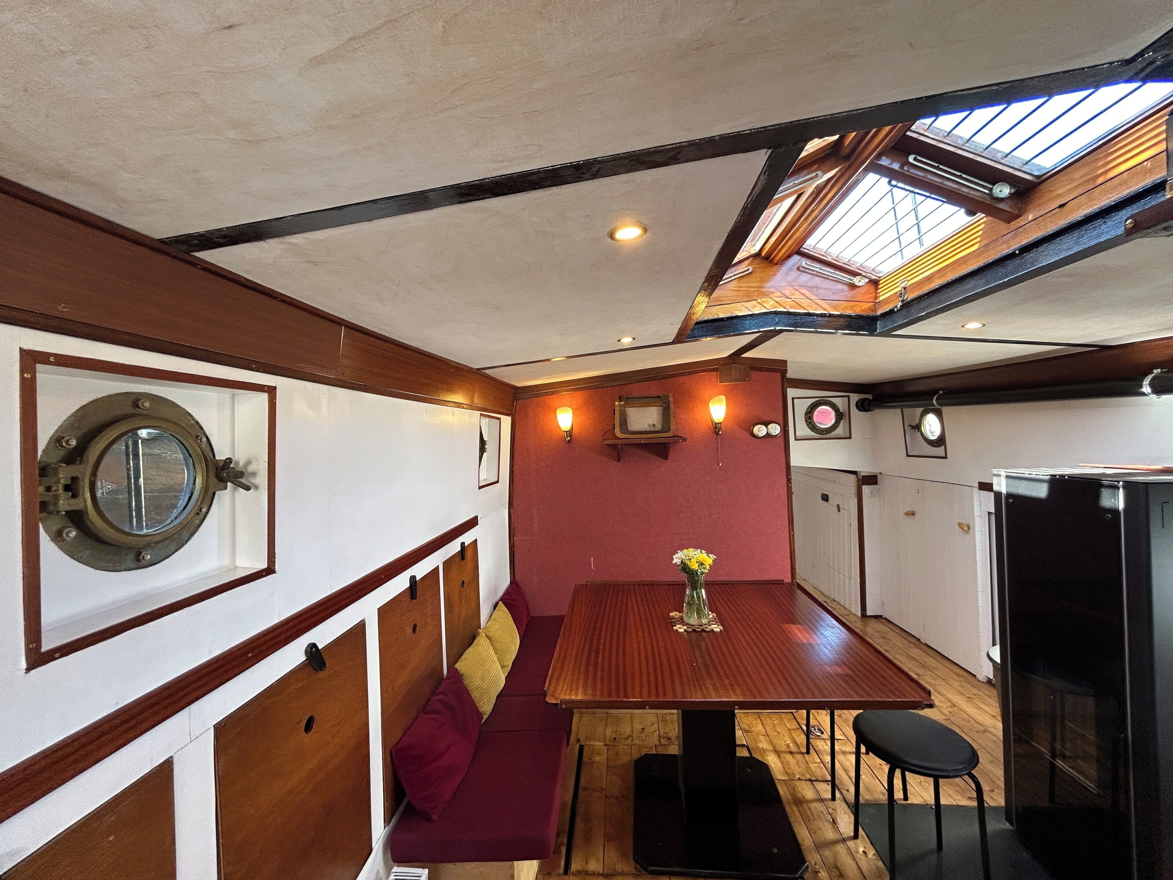 Ein gemütlicher, nautisch gestalteter Innenraum mit Holztisch, Sitzbank, Bullaugenfenster und Oberlicht.