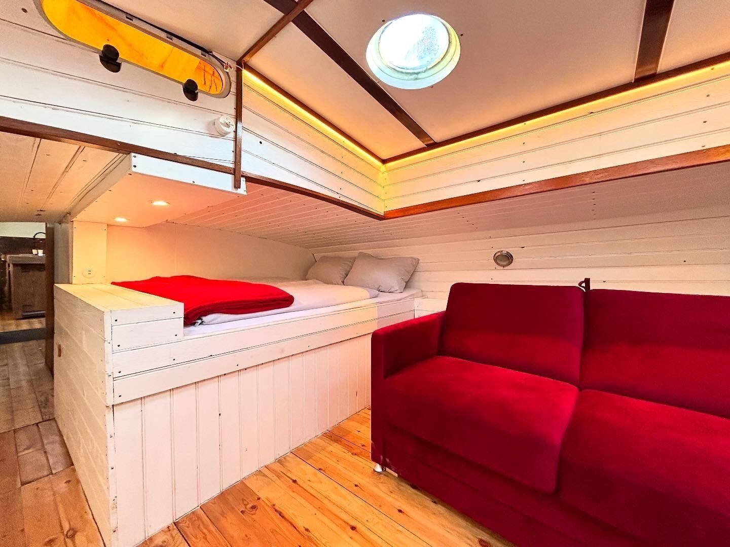 A compact room with a bed, a red sofa, a small table, and a ceiling light.