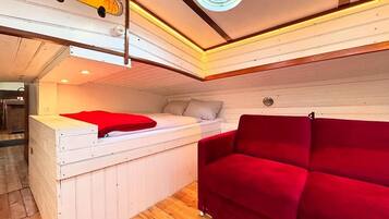 A compact room with a bed, a red sofa, a small table, and a ceiling light.