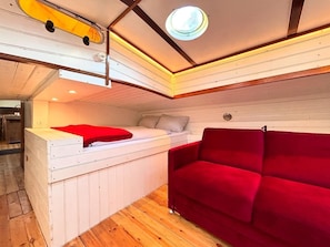 A compact room with a bed, a red sofa, a small table, and a ceiling light. - Hausboot Jonathan: Sanftes Schaukeln statt Alltagsstress (Hamburg)