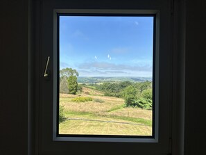 A window with a view of a hilly landscape, a clear sky, and two sailboats in the distance. - Large holiday cottage in West Wales with free entry to Bird of Prey Centre (Carmarthen)