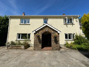 A two-story house with a stone archway entrance, multiple windows, and a front garden. - Large holiday cottage in West Wales with free entry to Bird of Prey Centre (Carmarthen)