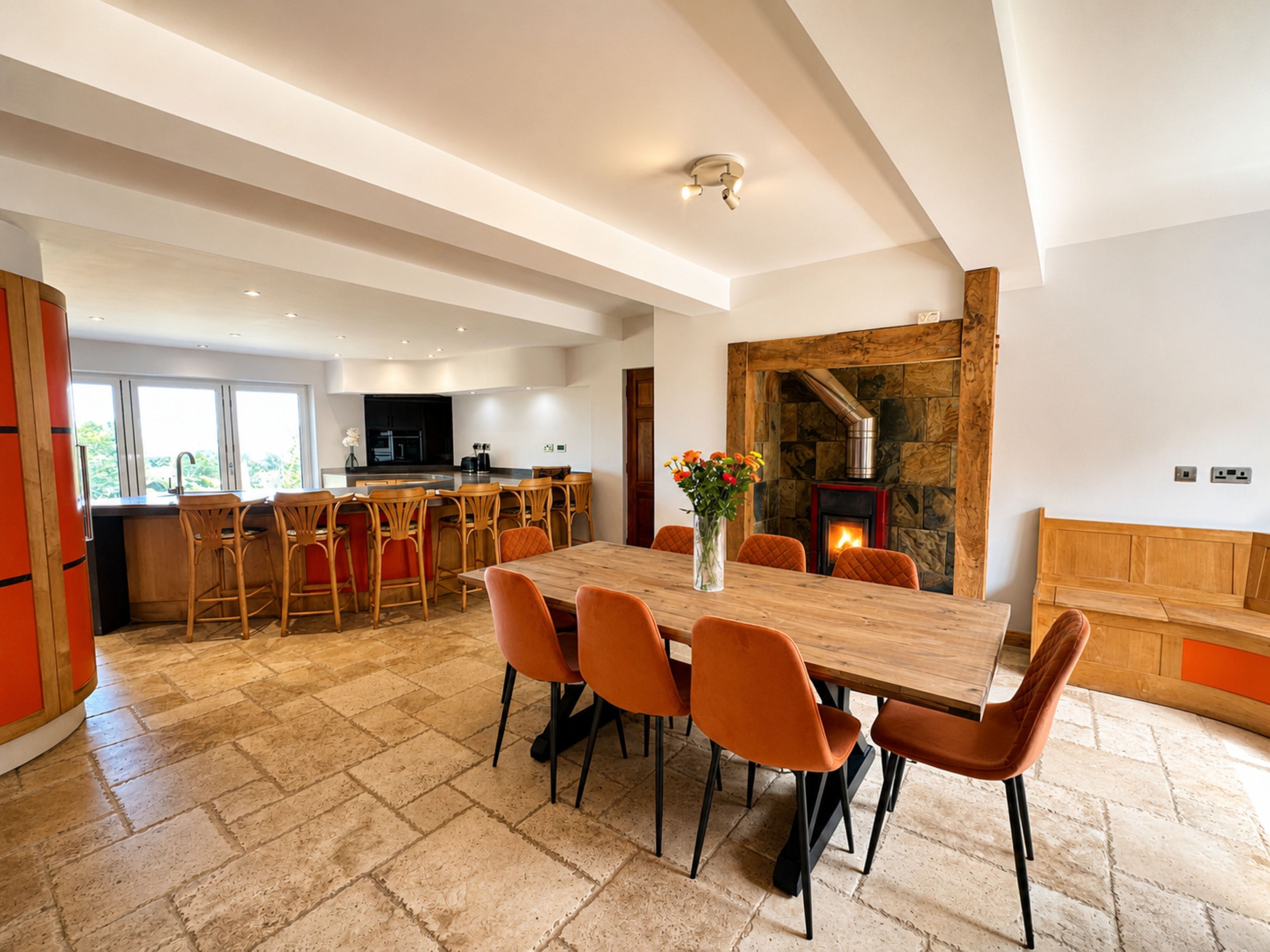A spacious kitchen with a dining area, a stone fireplace, and a large window.