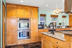 A kitchen with wooden cabinets, stainless steel appliances, granite countertops, and a window with a view of trees. - Stunning 4BR with Breathtaking Mountain Views -Sierra Hideaway (Groveland)