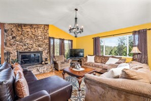 Una sala de estar con chimenea de piedra, sofás de cuero, televisor y candelabro.