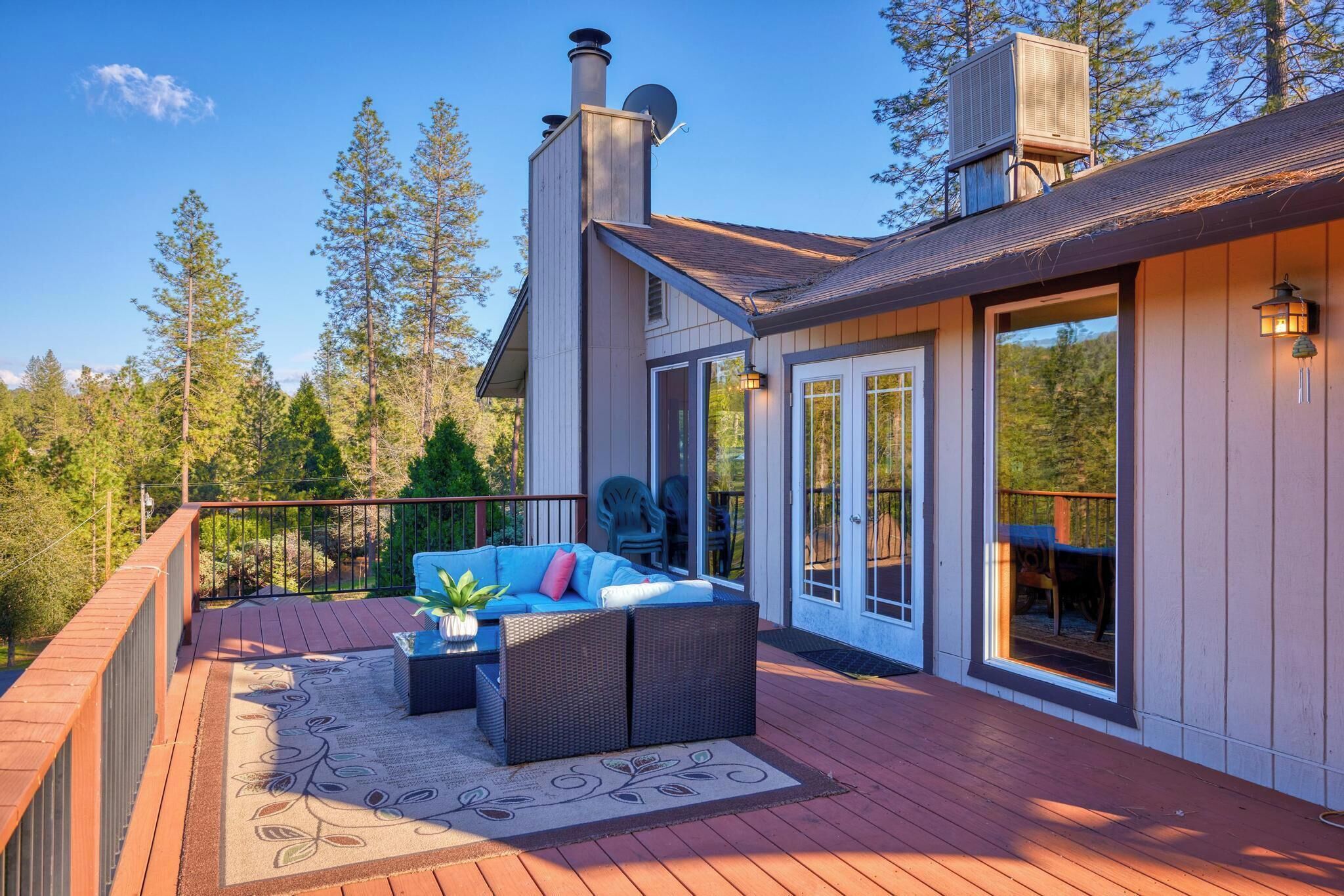 A deck with outdoor furniture, a chimney, and a large window overlooking a forest.