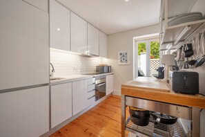 A modern kitchen with white cabinets, a microwave, an oven, and a wooden countertop. - GuestReady - Charming Lisbon Duplex Apartment (Lisbon)