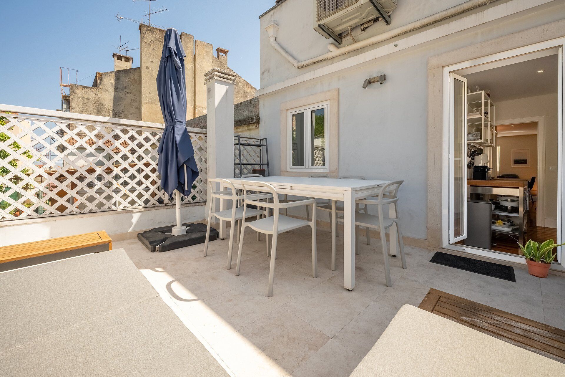 Un patio con una mesa y sillas blancas, una sombrilla azul y una valla blanca.