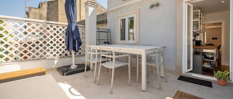 Un patio con una mesa y sillas blancas, una sombrilla azul y una valla blanca.