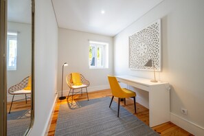 Ein Zimmer mit Schreibtisch, zwei Stühlen, einer Stehlampe, einer Wanddekoration mit Muster und einem Fenster.