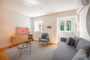 A modern living room with a sofa, a chair, a TV, and a small table. - GuestReady - Charming Lisbon Duplex Apartment (Lisbon)