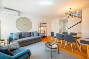 Ein modernes Wohnzimmer mit grauem Sofa, einem Couchtisch und einem Essbereich mit Stühlen und einem Glastisch.