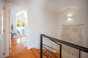 Eine Treppe mit schwarzem Geländer führt zu einem Raum mit weißer Wand und Wandbehang aus Makramee.