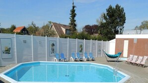 Una piscina rectangular amb vora enrajolada, envoltada per un mur de maó baix. Hi ha gandules i un hamaca a prop de la piscina.