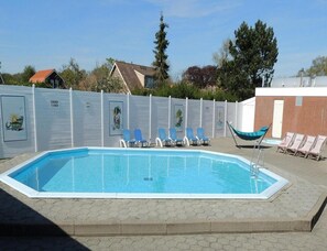 A rectangular swimming pool with a tiled edge, surrounded by a low brick wall. There are lounge chairs and a hammock near the pool. - Spacious Bungalow Near Oostkapelle for 4 (Oostkapelle)